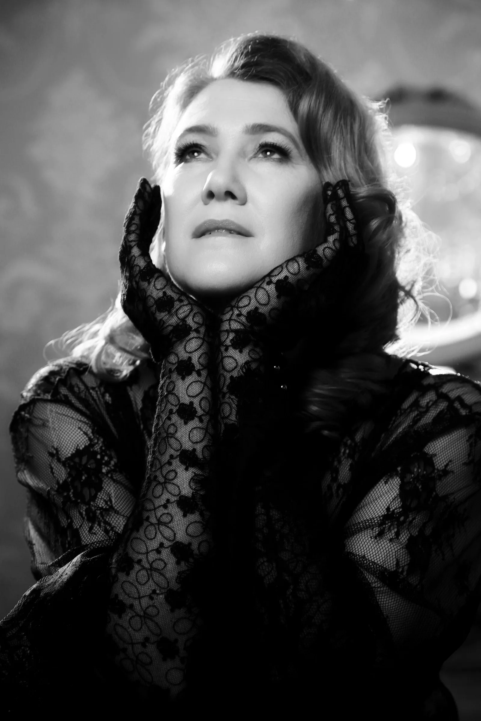 A black and white portrait of a client in lace gloves, her hands framing her face as she looks up