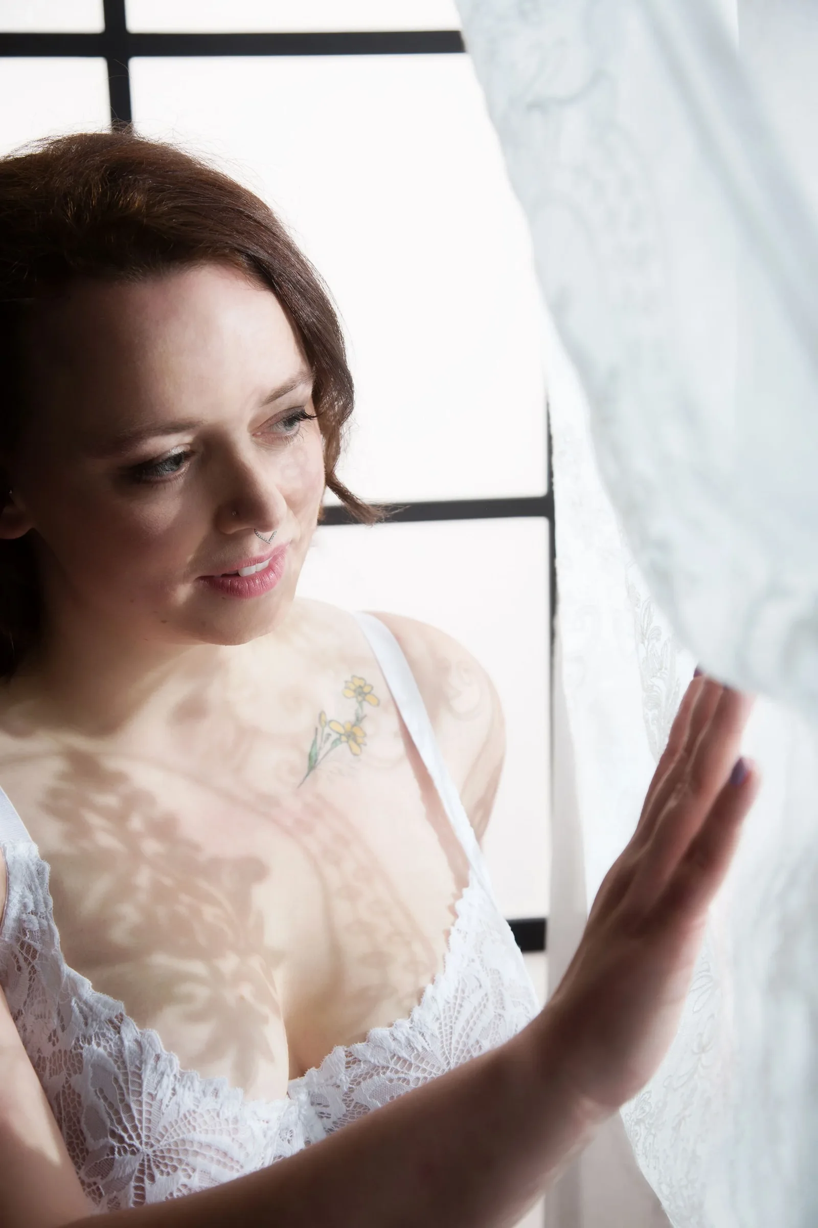 A bride smiling beside a studio window with a lace veil over her head