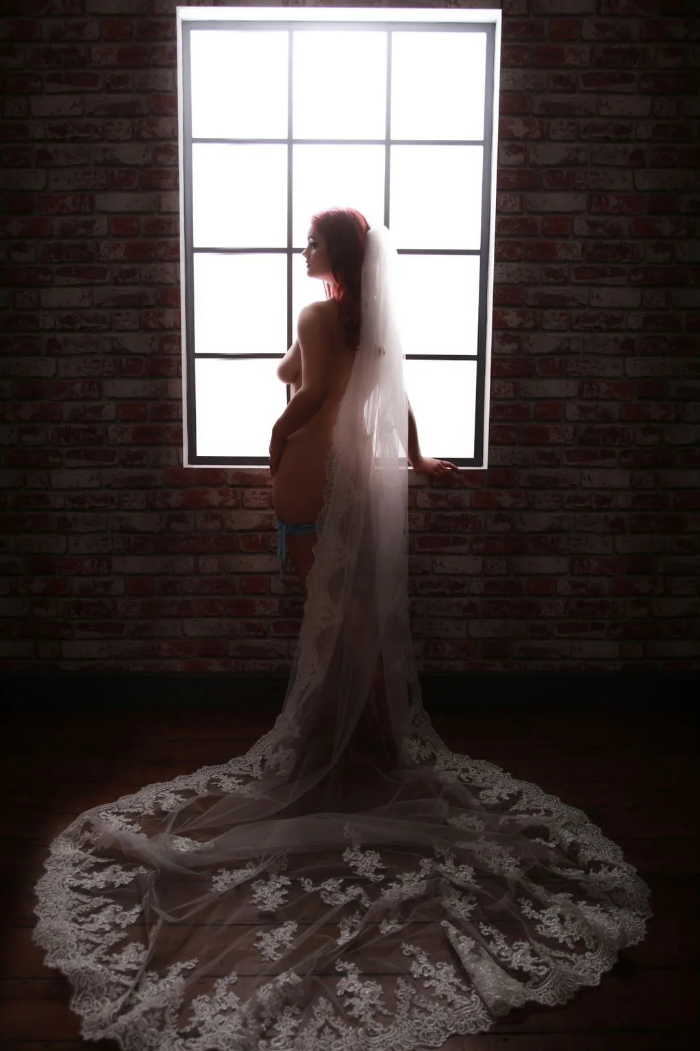 A client standing beside a studio window in a long white dress